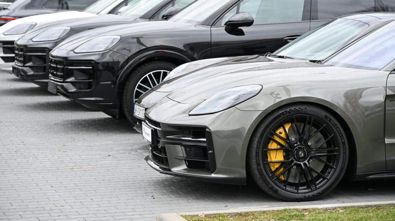 New Porsche cars in a dealer lot, green Panamera and 911 in the foreground, various Cayennes further away