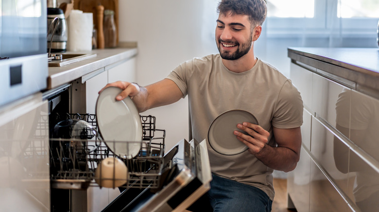 A person loading plates into a dishwasher