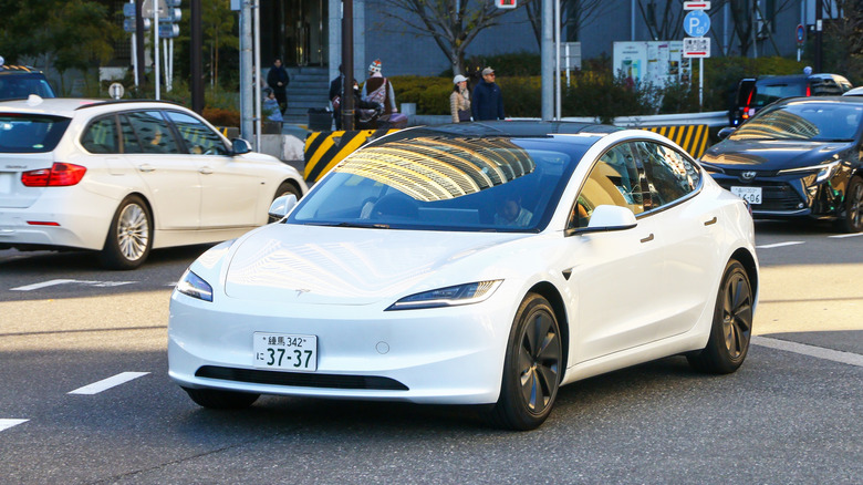 Front 3/4 of white Tesla Model 3 driving on Japanese city street.