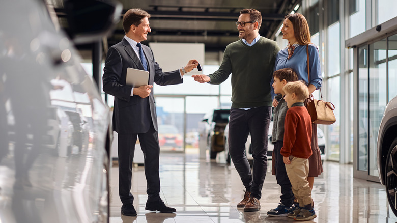 A smiling salesman handing over keys to a family of four inside a car dealership