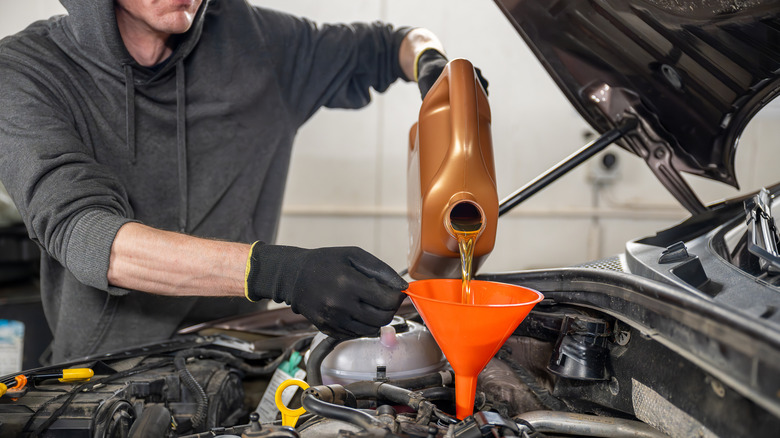 A mechanic wearing gloves pouring oil into a car engine using an orange funnel