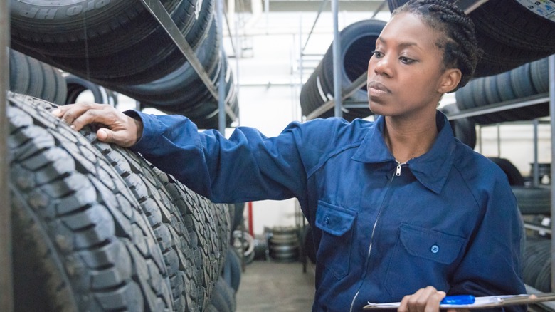 A tire technician inspecting new car tires stored on a rack.