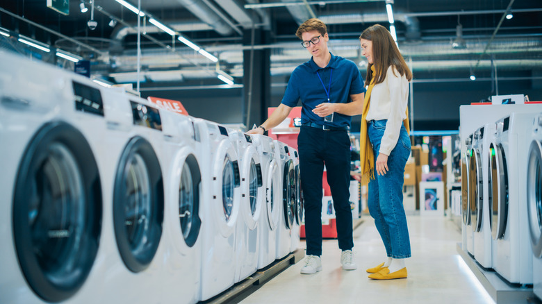 A male store employee in blue helping a woman in white select a washer or dryer