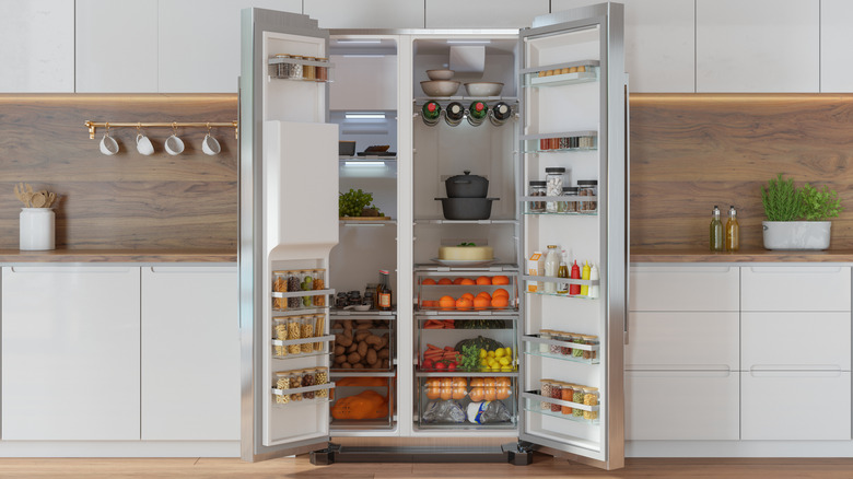 Modern kitchen interior with front view of open refrigerator filled with fruits, vegetables and various foods