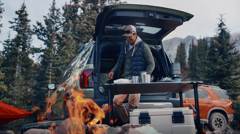 A person preparing drinks on the Honda Passport picnic table next to a campfire