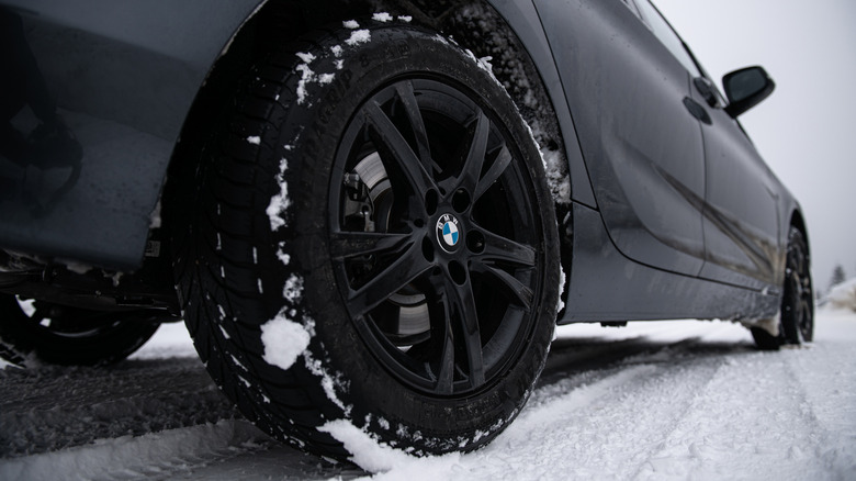 A close-up of a dark gray BMW wearing Goodyear tires in the snow.