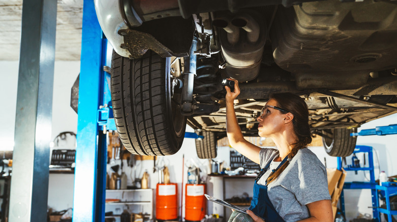 female mechanic inspecting the undercarriage of a vehicle