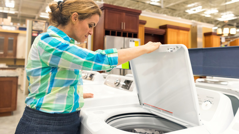 A woman looking into a top-loading washing machine at a store