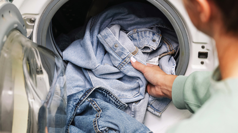 A person loading denim clothes into a front-loading washing machine