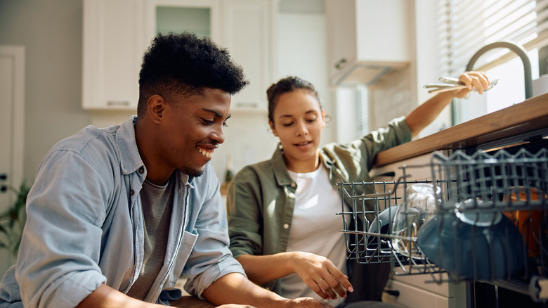 A couple loading up a dishwasher on a sunny day