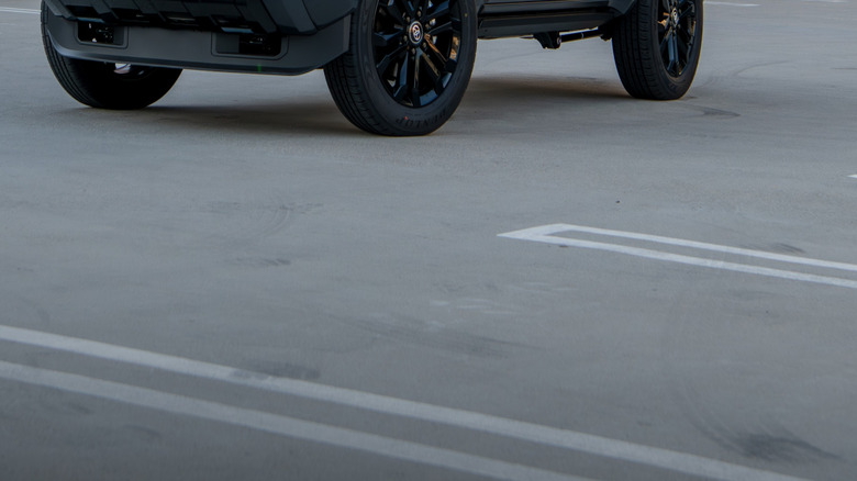 A blocky black SUV parked outside the bays, in the middle of an empty car park, with its lights on, but no-one behind the wheel