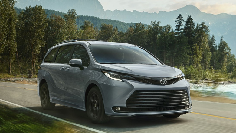 Front 3/4 view of Toyota Sienna Woodland hybrid minivan in mountainous setting, driving past a stream