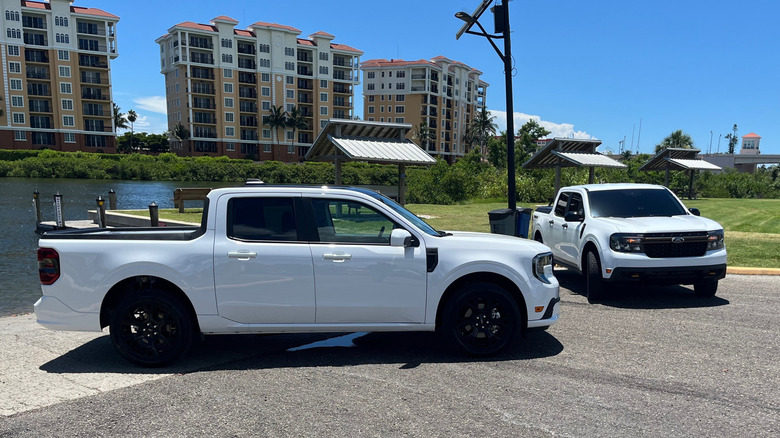 Side view of two white Ford Maverick pickups parked in front of marina.