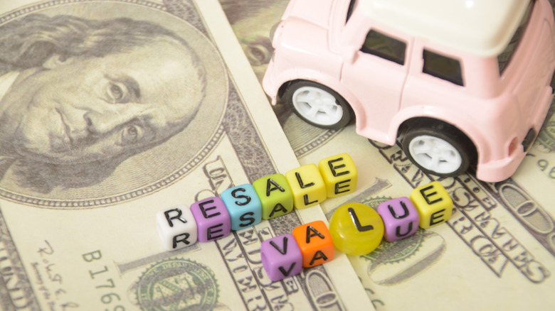 A pink toy car sitting on top of 100 dollar bills and the words 