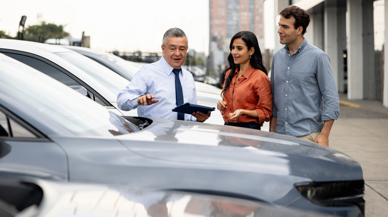 A car dealer showing off a car to a couple