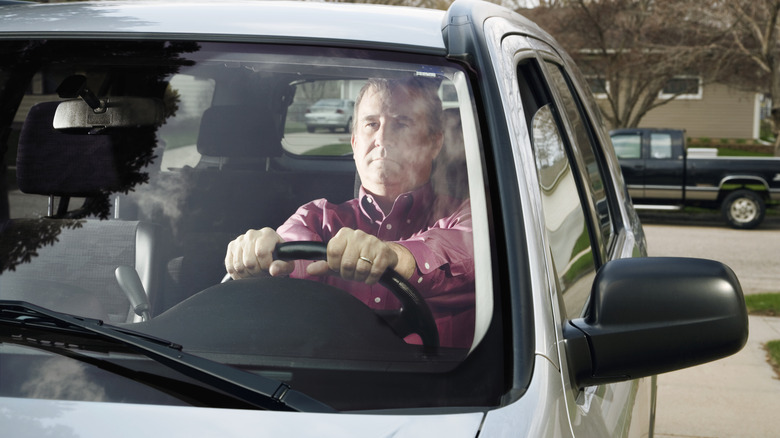 Man sitting behind the steering wheel of his car looking through the windshield.