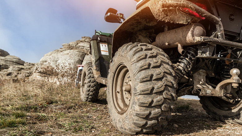 Close-up of ATV from the rear, showing tire and mud-caked undercarriage.