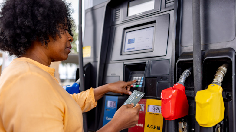 A woman refueling her car at a gas station and paying by card