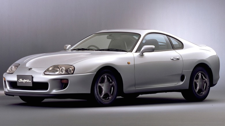 A 1993 silver Toyota Supra GZ with factory five-spoke wheels and the iconic "Supra" script on the front bumper is being displayed against a neutral studio gradient background.