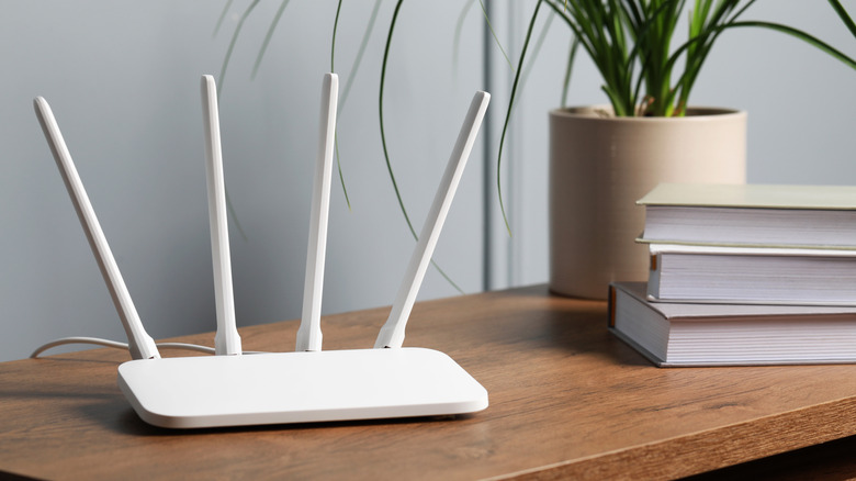 white router with four antennas placed on a wooden table alongside books and a plant