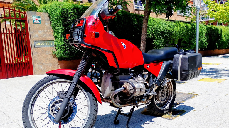 A BMW R80 G or S red motorcycle parked on the walkway in front of a house.