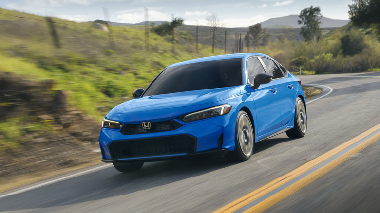 A blue 2026 Honda Civic Hybrid on the move on a mountain road, front 3/4 view