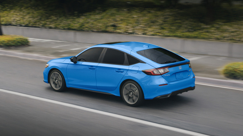 A blue 2026 Honda Civic Hybrid on the move on an urban road, rear 3/4 view