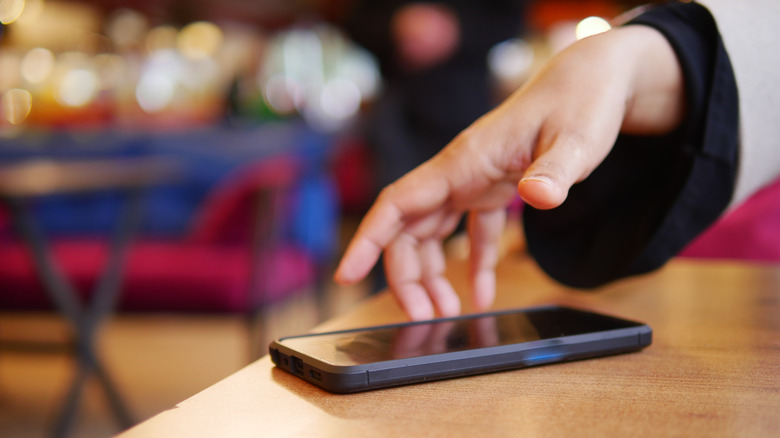 A person's hand reaching for a smartphone on a table