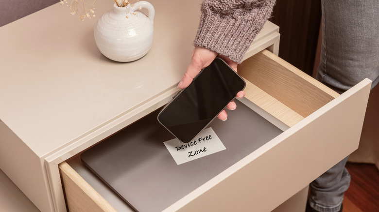 A woman placing a smartphone into a drawer with a note inside that says, "Device Free Zone."