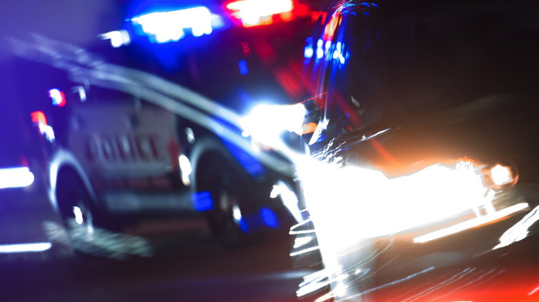 A police car with flashing lights chasing a fast car at night
