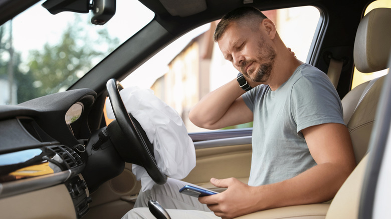 Man sitting in car holding his neck with a deployed airbag in front of him