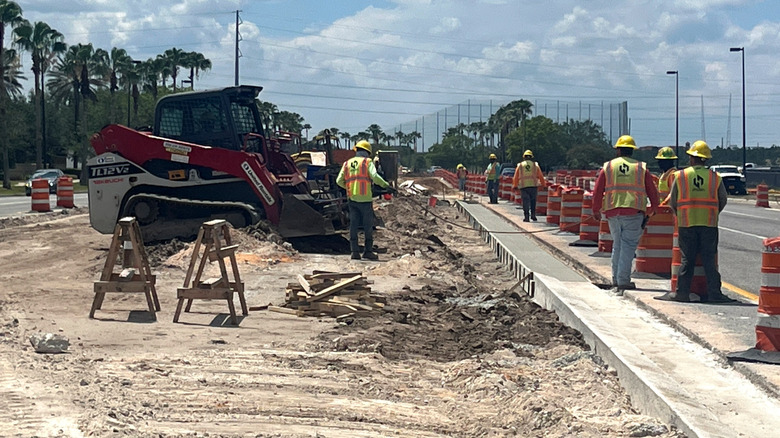 Construction workers paving road with palm trees in background