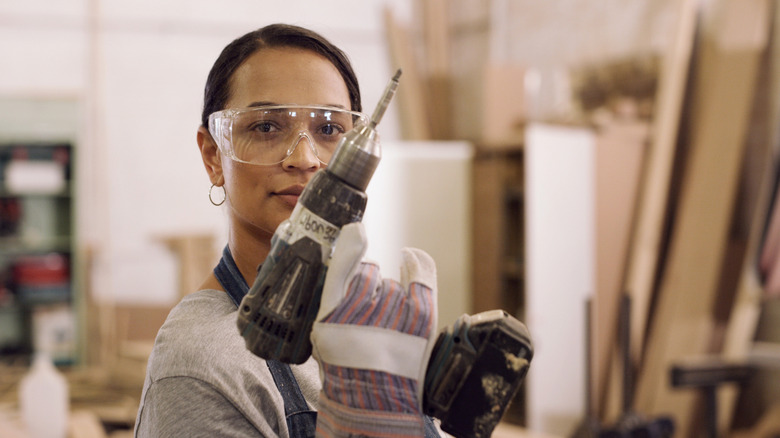 woman wearing eye protection and gloves while holding a drill