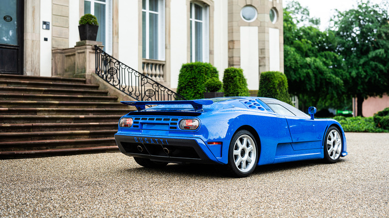 Blue Bugatti EB110 hypercar seen from right rear parked in fron of luxury house