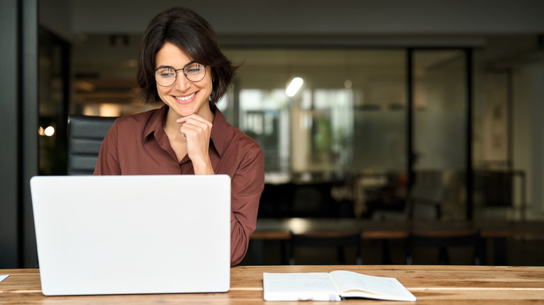 Woman with glasses looking at laptop screen while smiling