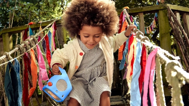 Child holding speaker while playing on a wooden treehouse