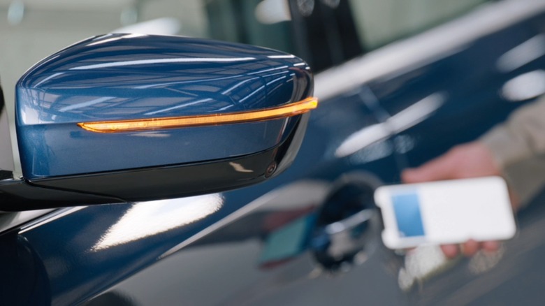 Car side mirror blinks light with iPhone placed at door handle in background
