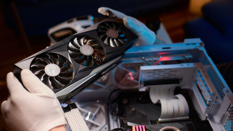 A person wearing gloves installing a GPU into a desktop tower
