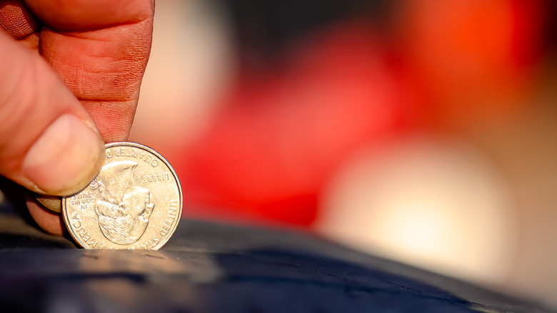 Man testing tire tread depth with quarter