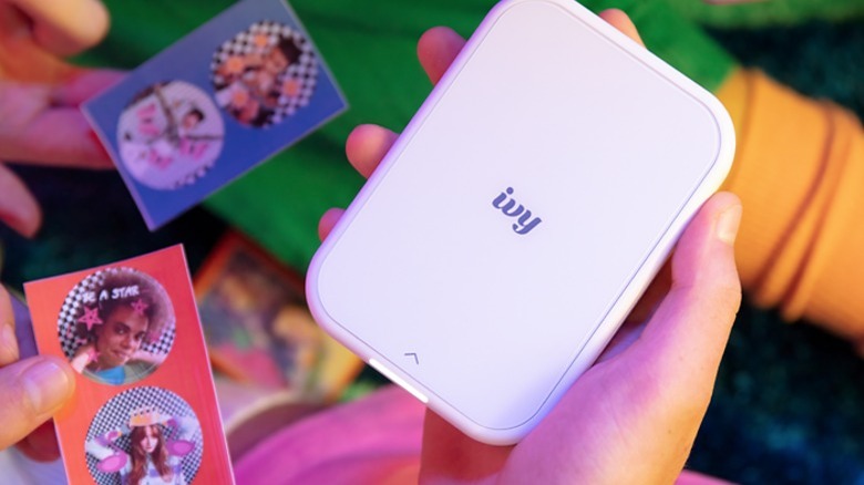 Person holding a white Canon IVY 2 mini printer and circular prints