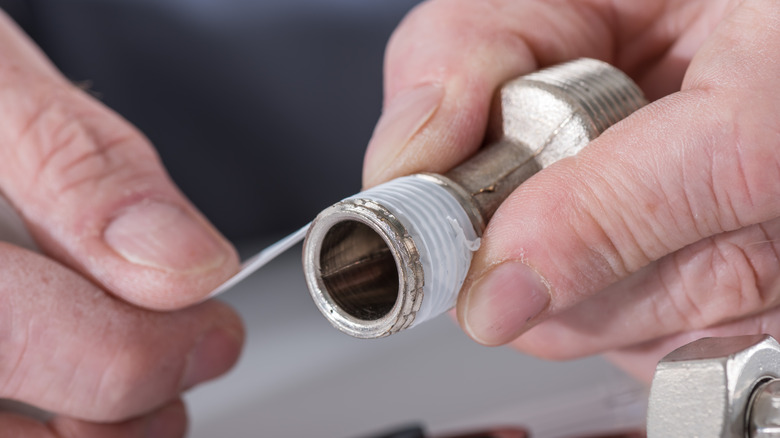 A close-up shot of the plumber's hands putting a teflon joint on a thread.