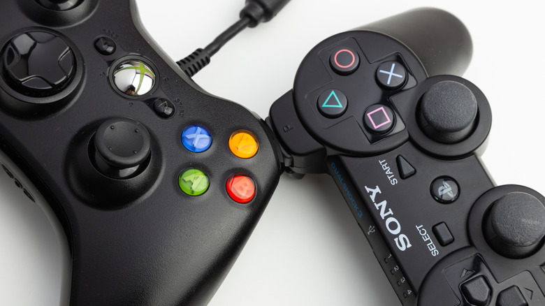 A close-up of a PS3 and Xbox 360 controller on a white surface.