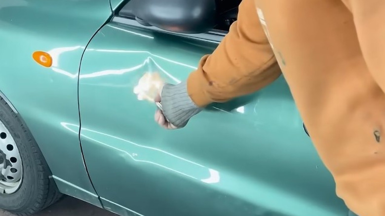 A man lights a car door on fire to fix a dent