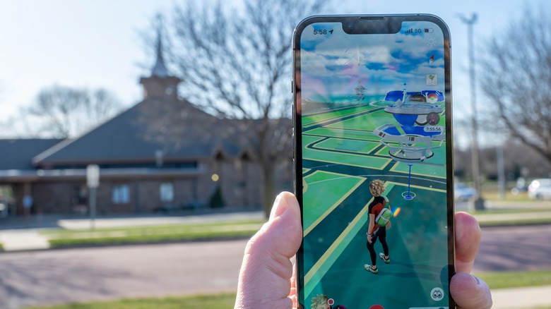 Pokemon Go game app on a phone with a defocused gym in the background.