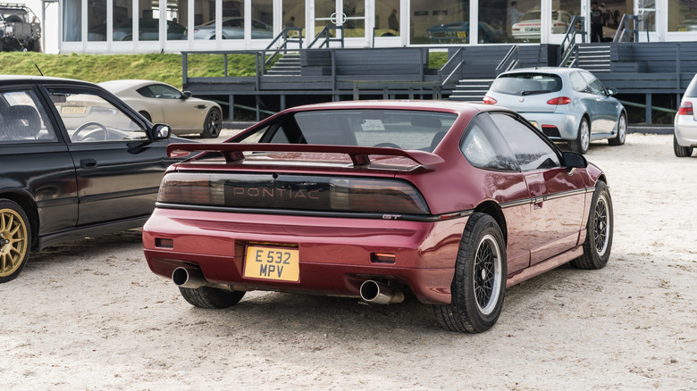 A red Pontiac Fiero on UK plates at a classic car show, rear 3/4 view