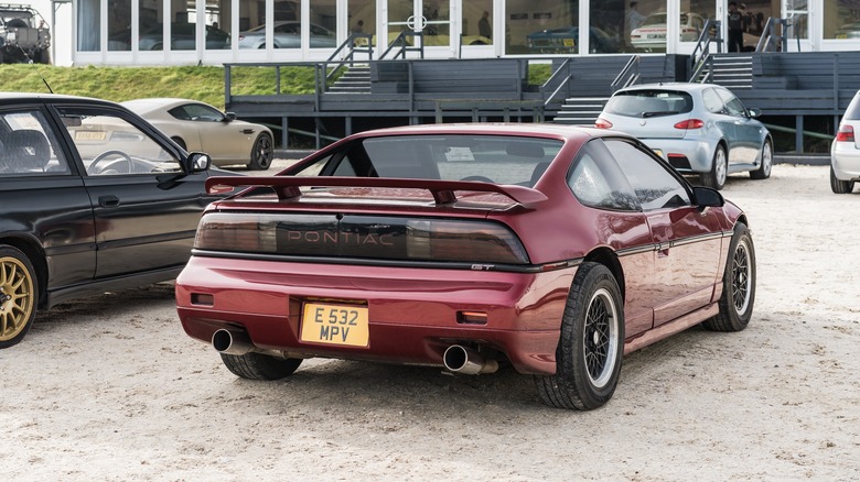 A red Pontiac Fiero on UK plates at a classic car show, rear 3/4 view