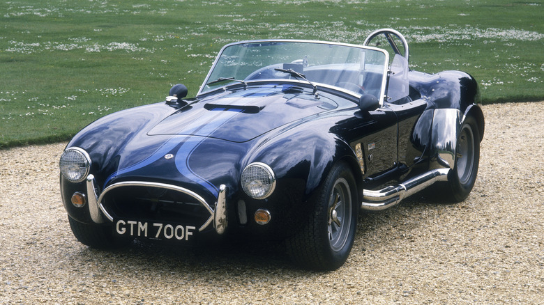 Blue Shelby Cobra parked on gravel in front of grass