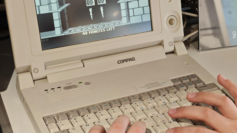 Close-up of hands typing on Compaq computer with screen displaying video game.