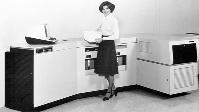 Woman holding stack of paper in front of a laser printer