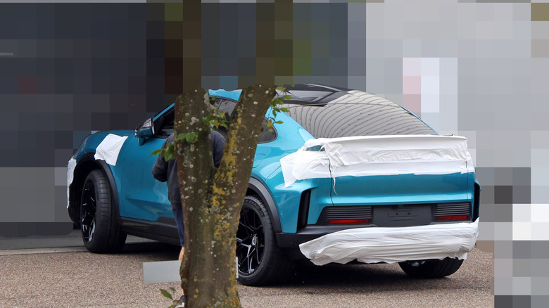 Spy shot of unreleased Porsche Cayenne Turbo Coupe with blurred background, rear-right 3/4 view, partially obscured by tree